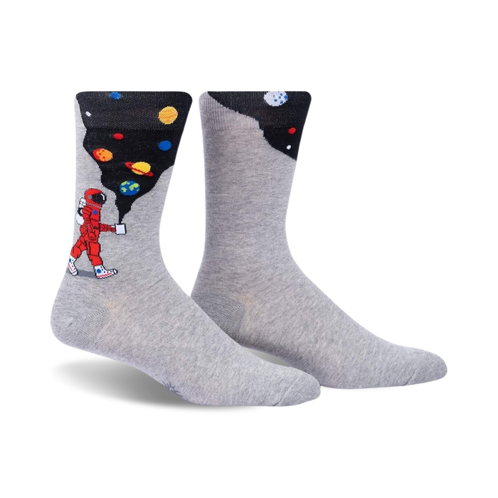 Pair of grey crew socks with a design featuring an astronaut painting planets onto a dark background.