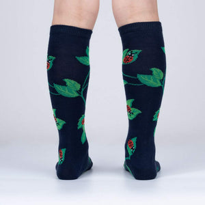 A pair of dark blue knee-high socks with a pattern of green leaves and red ladybugs.