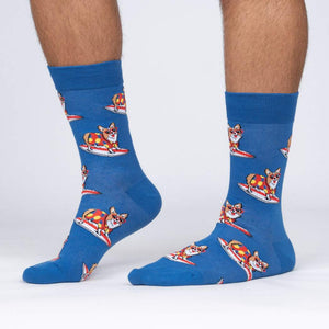 Lifestyle shot: Person wearing blue crew socks with a pattern of corgis surfing.