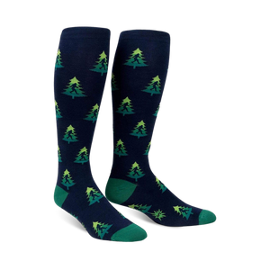 Pair of navy blue knee-high socks with a repeating pattern of green Bigfoot figures hidden amongst lime green and darker green Christmas trees.