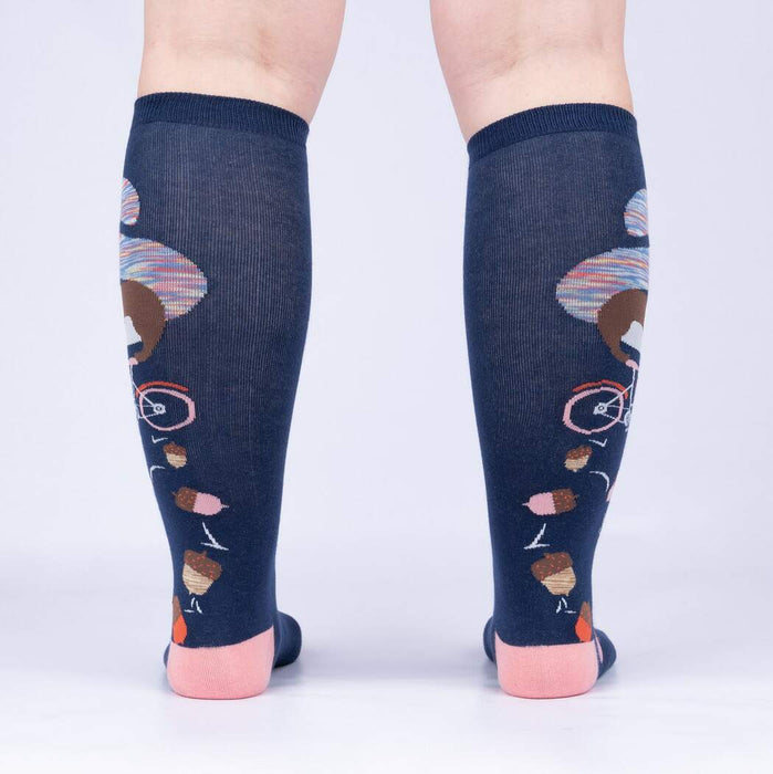 A pair of knee-high socks with a pattern of cartoon chipmunks riding bicycles on a navy blue background. The socks have pink toes and heels.