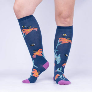 A pair of blue knee-high socks with a pattern of hummingbirds, bees, and orange trumpet lilies.