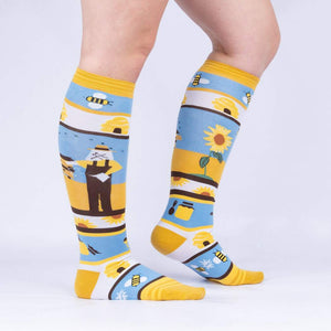 Yellow knee-high socks with a pattern of sunflowers, beehives, and bees on a blue background.