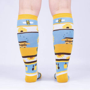 Yellow knee-high socks with a pattern of sunflowers, beehives, and bees on a blue background.