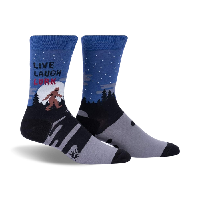 Pair of crew socks in blue, gray, and black, showing a Bigfoot design in a snowy forest scene with the text 'Live, Laugh, Lurk'.