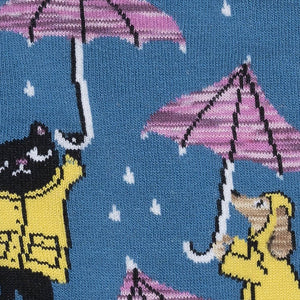 Close-up detail shot highlighting the sock's playful design: cats, dogs, umbrellas, and rain.