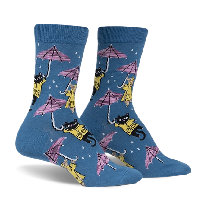 Pair of blue crew socks with a repeating pattern of black cats and dogs in yellow raincoats holding pink umbrellas in the rain.