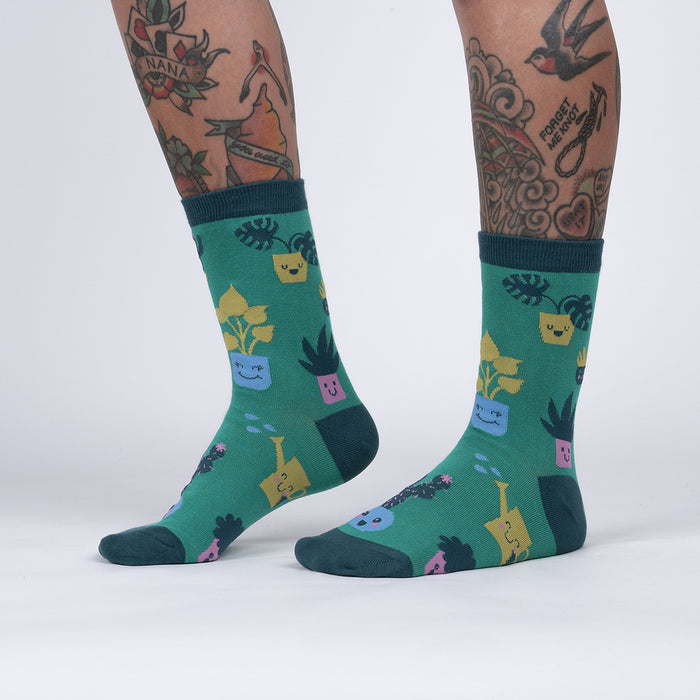 A pair of green socks with a pattern of potted plants with smiley faces on them.