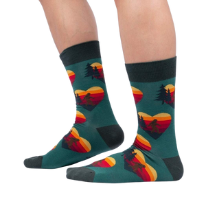A pair of green socks with a pattern of red, orange, and yellow hearts. The hearts have a silhouette of a sasquatch inside them, along with pine trees and a mountain range.