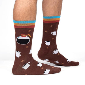 A pair of brown socks with a pattern of white coffee cups and brown coffee beans. The top of the sock is brown with a blue, yellow, and orange stripe.
