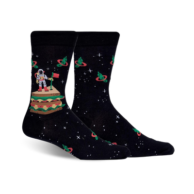 Pair of black crew socks with an astronaut on a sandwich in space, surrounded by orbiting pickles. Red, green, and white details against a dark background.