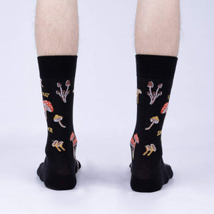 Rear view of the 'Let That Shiitake Go' socks on a model's feet.  The socks are black with a mushroom and pun design.