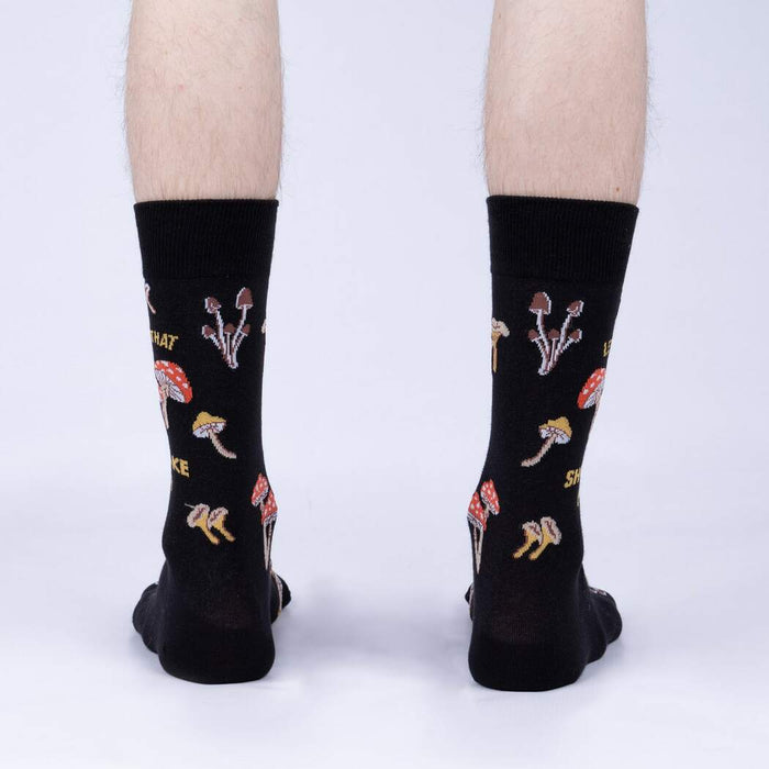 Rear view of the 'Let That Shiitake Go' socks on a model's feet.  The socks are black with a mushroom and pun design.
