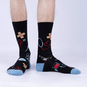 A pair of black socks with a light blue toe and heel. The socks have a pattern of medical symbols, including a stethoscope, pills, and a DNA double helix.