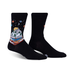 Pair of black crew socks featuring a whimsical design of a book with a mountain landscape inside, set against a starry night sky with planets.