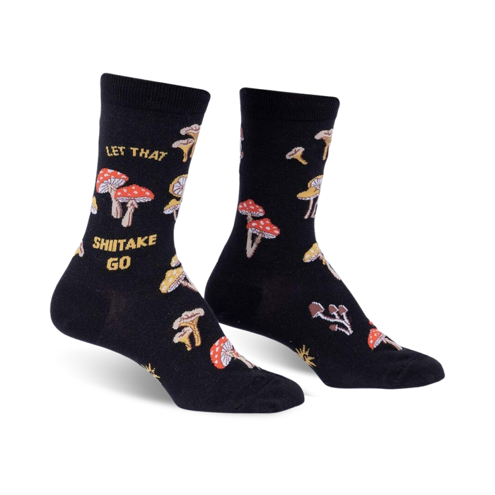 Pair of black crew socks with a whimsical mushroom and 'Let That Shiitake Go' design. Red and gold mushrooms are scattered across the black fabric.