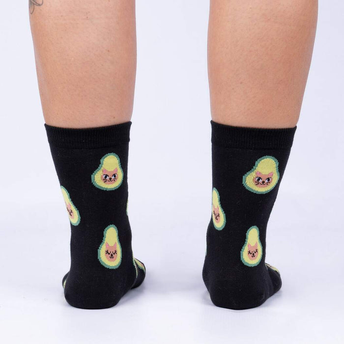 A pair of black socks with a pattern of green avocados with cat faces on them.