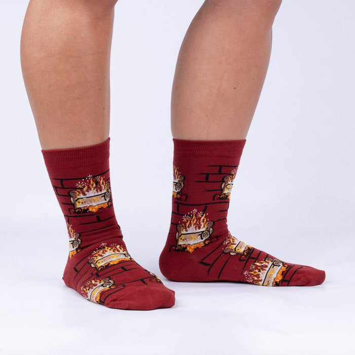 A pair of red socks with a pattern of cartoonish logs on fire set against a brick background.