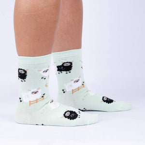 A pair of light green socks with a pattern of black and white sheep.