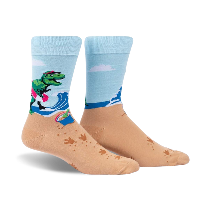 Crew socks in light blue and tan. Design features a T-Rex on a surfboard at the beach with wave and footprint details.