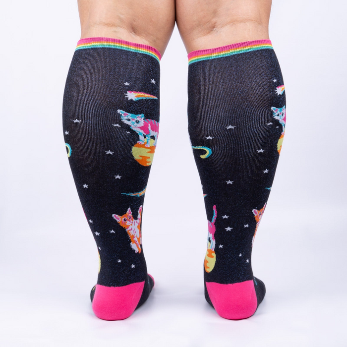Rear view of Space Cat knee-high socks on a person's legs.  Full view of the sock pattern and bright pink heel.