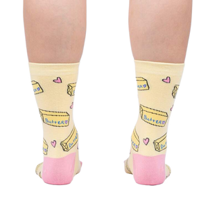 Rear view of the socks on a person's legs, highlighting the pink heel and toe details against the pastel yellow.