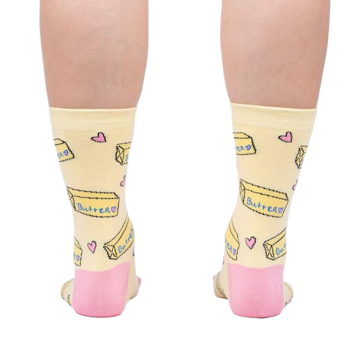 Rear view of the socks on a person's legs, highlighting the pink heel and toe details against the pastel yellow.