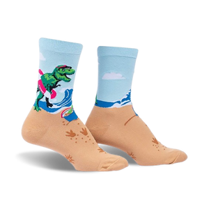 A pair of crew socks showcasing a T-Rex surfing on a beach.  The socks are light blue and tan with green, pink, and white accents.