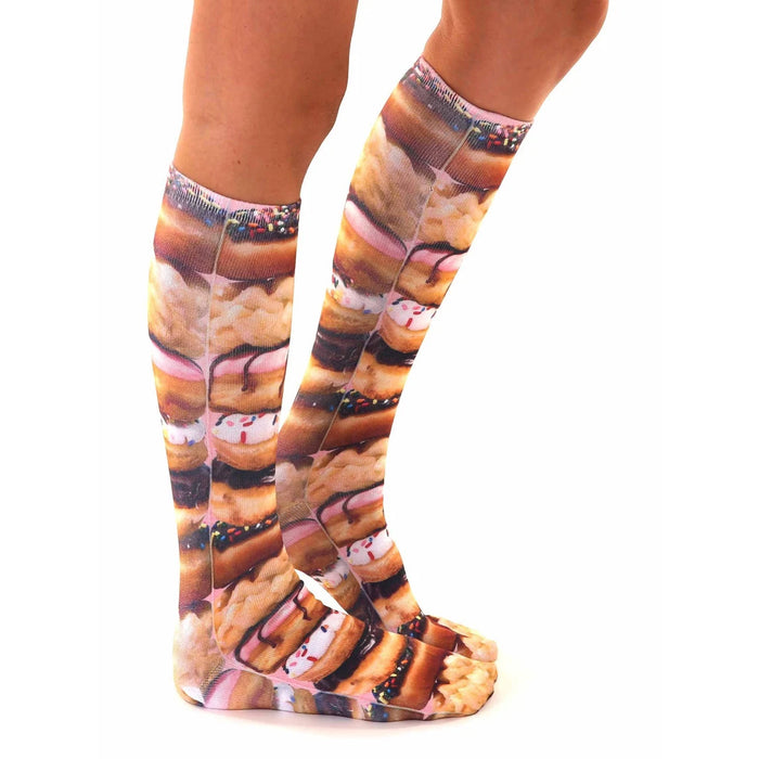 A pair of legs is shown from the knees down. The person is wearing socks that have a pattern of donuts on them. The donuts are pink, brown, and tan in color and have white and brown frosting on them.