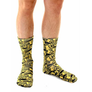 Another lifestyle shot of a person wearing the 'Caution' socks. Shows a different angle of the socks on the model's legs.
