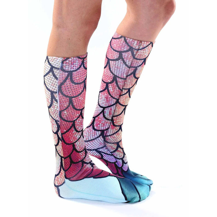 A pair of calf-length socks with a mermaid tail pattern. The socks are white at the top and have a blue-green scale pattern that transitions to pink at the bottom.