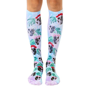 Pair of pastel blue knee-high socks with a repeating pattern of skulls adorned with red roses and tropical leaves.