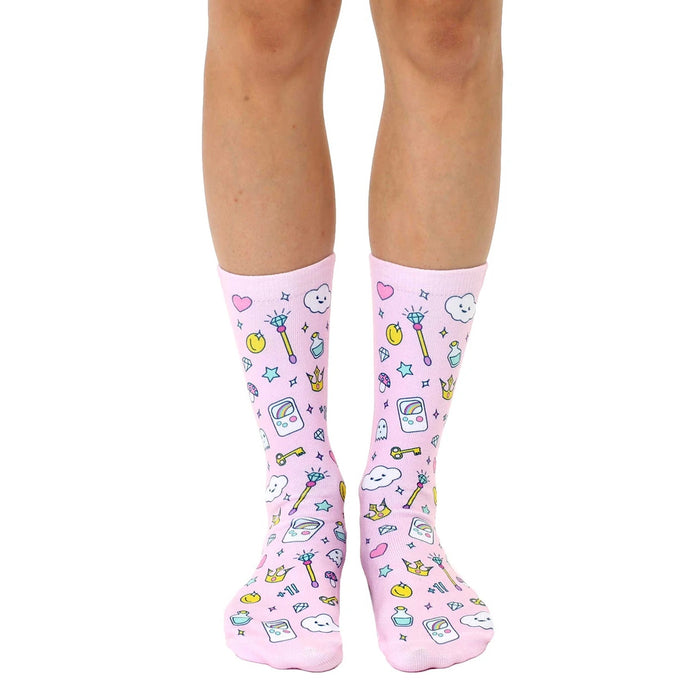 A pair of women's crew socks on a white background.  They're pink with a fun pattern of cartoon magic wands, crowns, and game controllers.