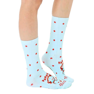 Lifestyle shot of a person wearing the light blue crew socks with red stars and a humorous parenting quote.