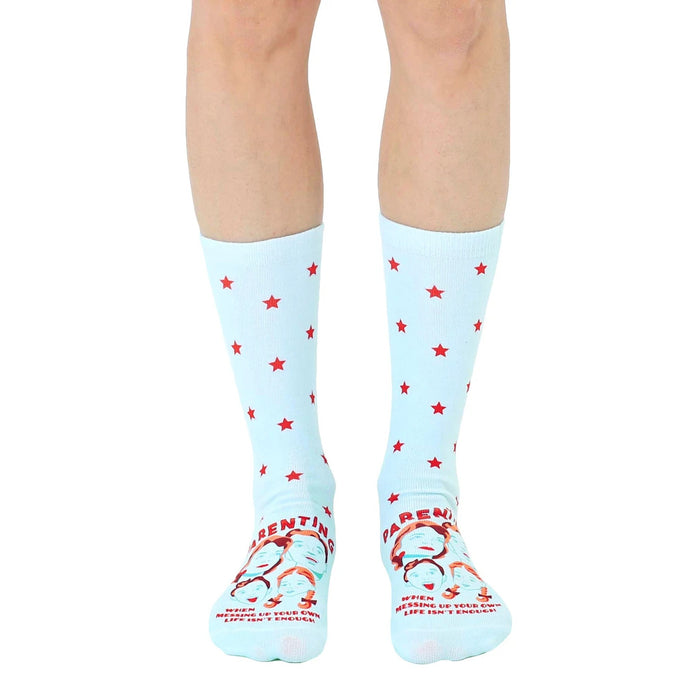 A pair of light blue crew socks with red stars and a humorous parenting quote featuring illustrated faces at the bottom.