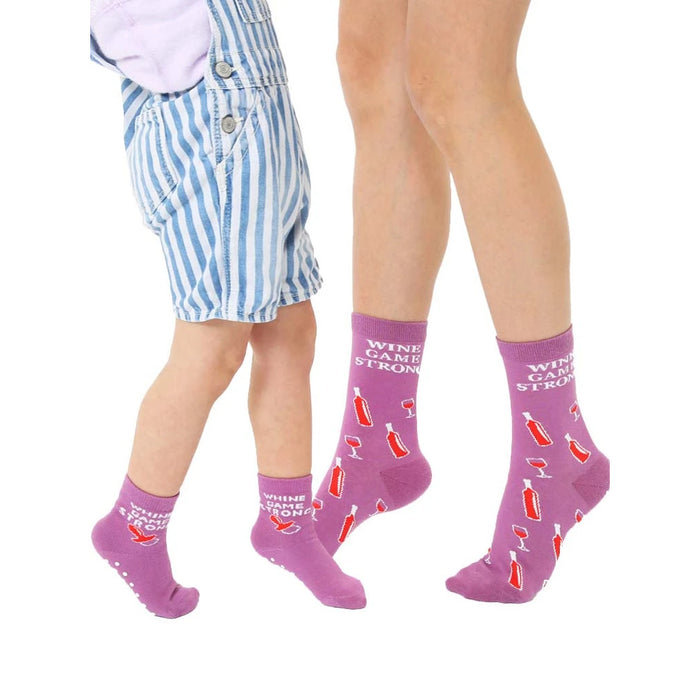 Adult and child crew socks in purple.  They feature a repeating pattern of wine bottles, wine glasses, and the text 'Wine Game Strong'.