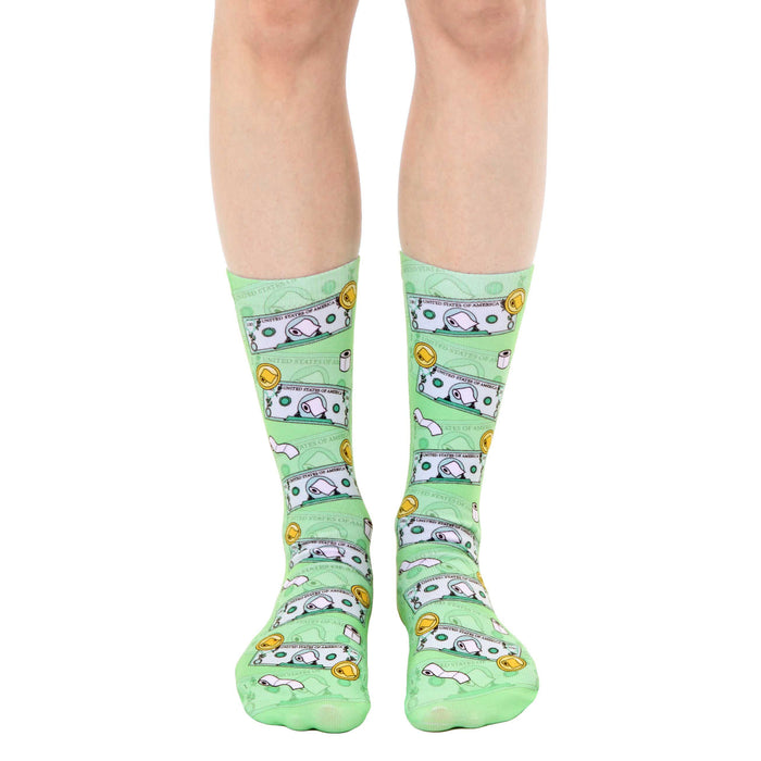 A pair of light green crew socks with a whimsical design featuring cartoonish dollar bills and toilet paper rolls.
