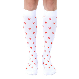 Pair of white knee-high socks with a repeating pattern of small red hearts.