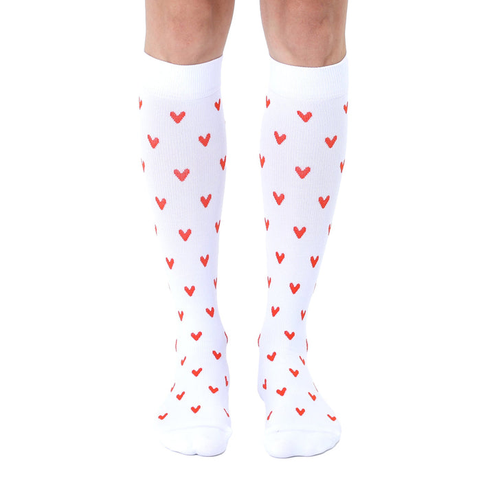 Pair of white knee-high socks with a repeating pattern of small red hearts.