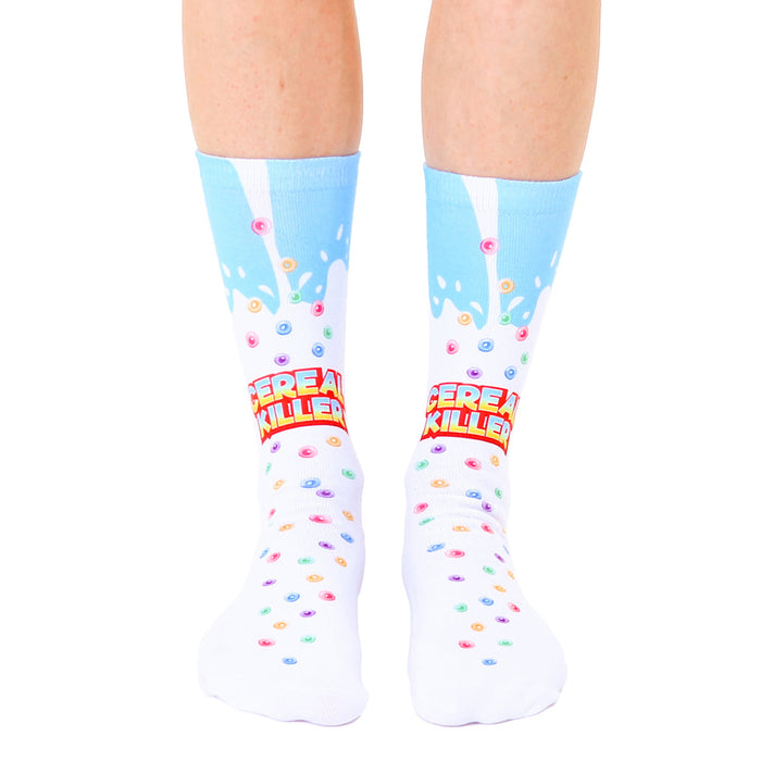 A pair of white crew socks with a light blue milk splash design and colorful cereal pieces. The text 'Cereal Killer' is prominently displayed.