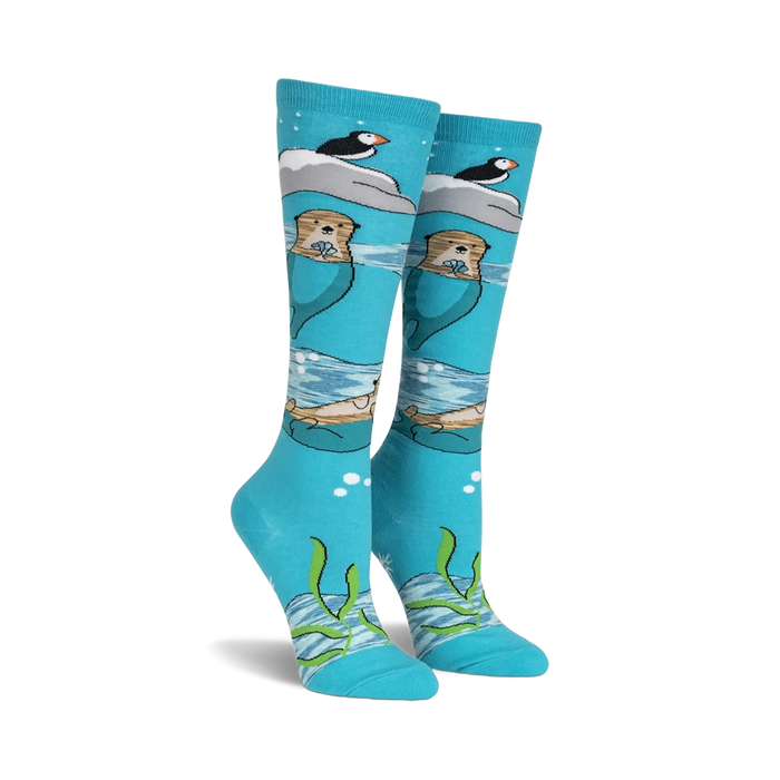 Pair of teal knee-high socks featuring otters, puffins, and icebergs.  Space dye yarn creates a whimsical, underwater scene.