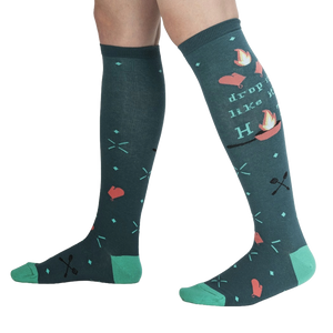 Lifestyle shot showing the 'Drop It Like It's Hot' socks on a person's legs.  The teal and green colors pop against the dark background.