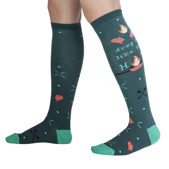Lifestyle shot showing the 'Drop It Like It's Hot' socks on a person's legs.  The teal and green colors pop against the dark background.