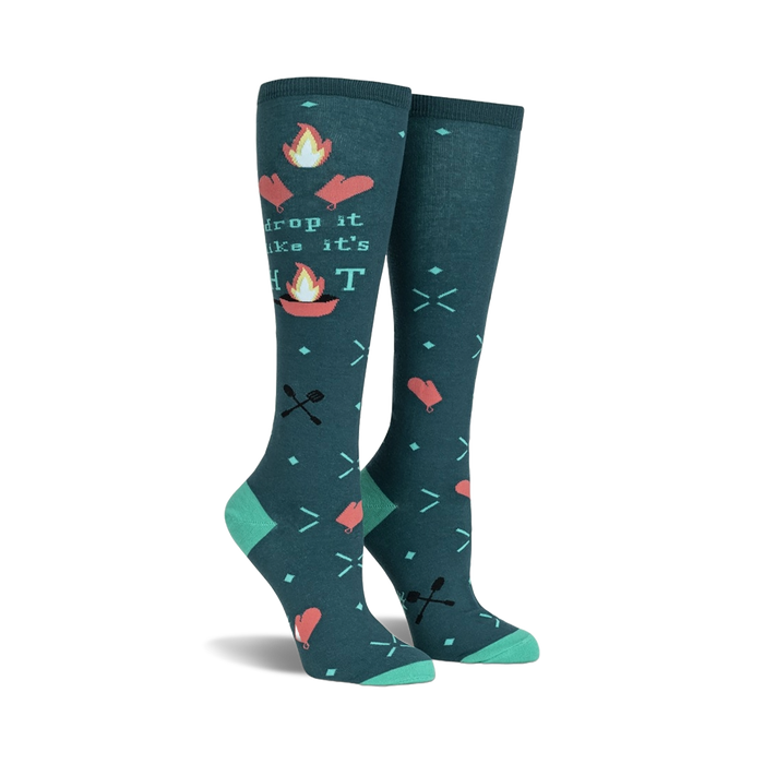 Pair of teal knee-high socks with a 'Drop It Like It's Hot' design. Campfire graphics, flaming hearts, and crossed utensils are featured on a teal background.
