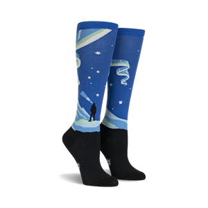 Pair of knee-high socks showcasing a Northern Lights design. Blue, green, and black colors are featured, along with a silhouette of a person watching the lights.