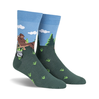 Crew socks in blue and green, depicting a cartoon Bigfoot relaxing in a wooden chair outdoors with a pot and bottles beside him.