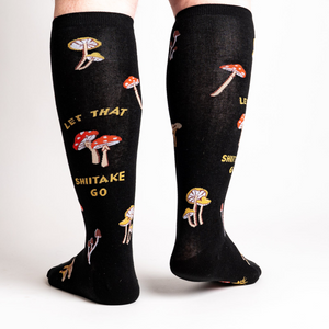 Back view of the 'Let That Shiitake Go' knee-high socks on a person's legs.  The socks show the full design, including the mushroom pattern and text.