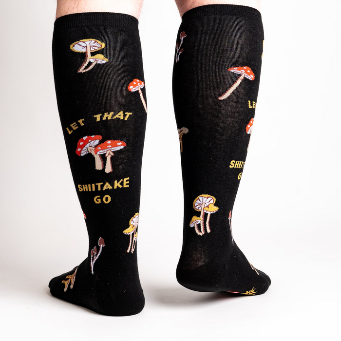 Back view of the 'Let That Shiitake Go' knee-high socks on a person's legs.  The socks show the full design, including the mushroom pattern and text.