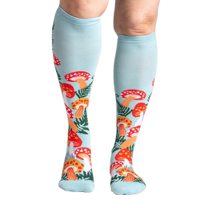A pair of blue knee-high socks with a pattern of red and orange mushrooms and green leaves on a light blue background.