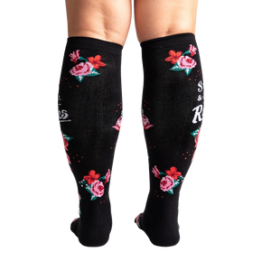 A pair of black knee-high socks with a red and pink floral pattern and the words 
